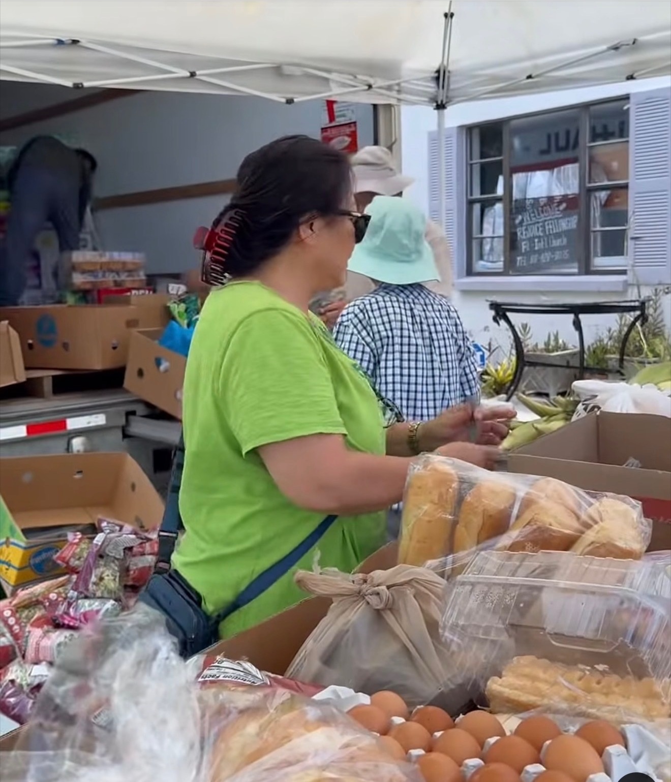 Boxes of bread and eggs set out under a white canopy tent at a Hands to the Needy food distribution