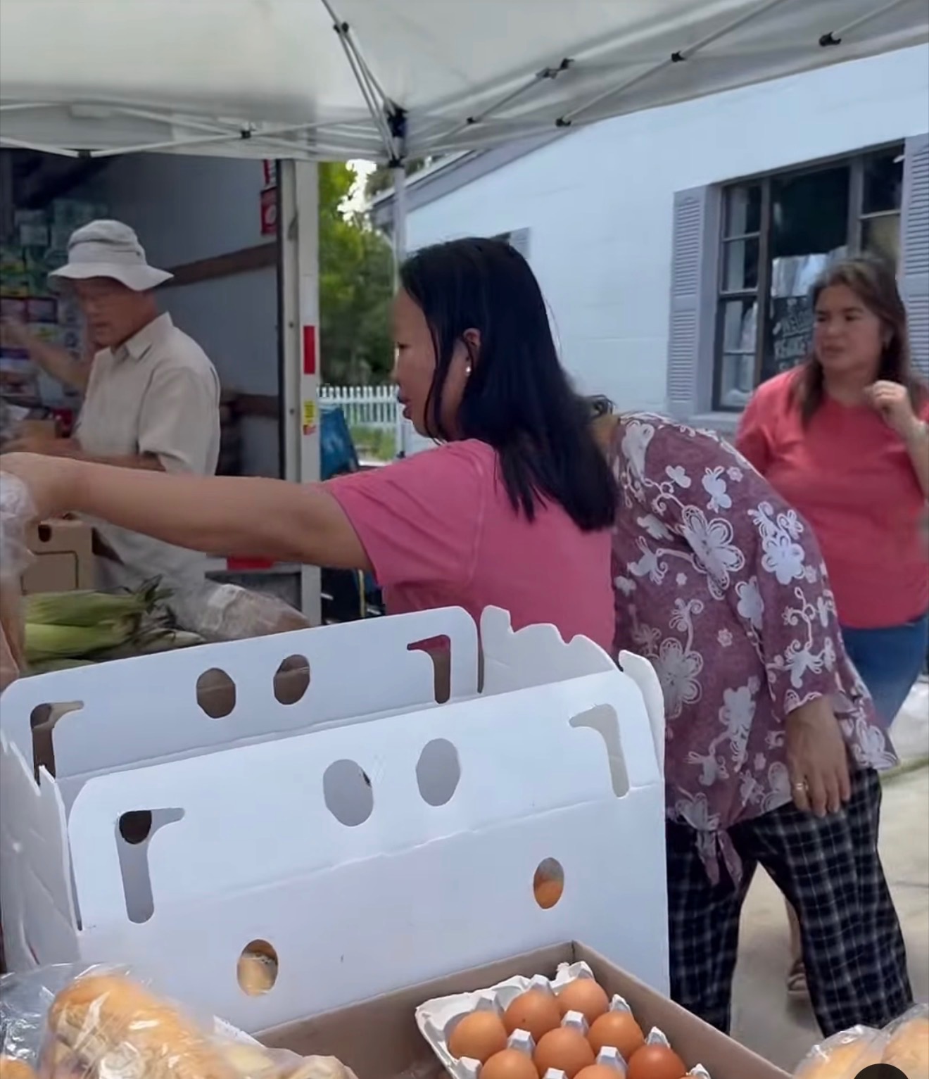 A volunteer reaches into a grocery box beside cartons of eggs and bags of bread at a food distribution
