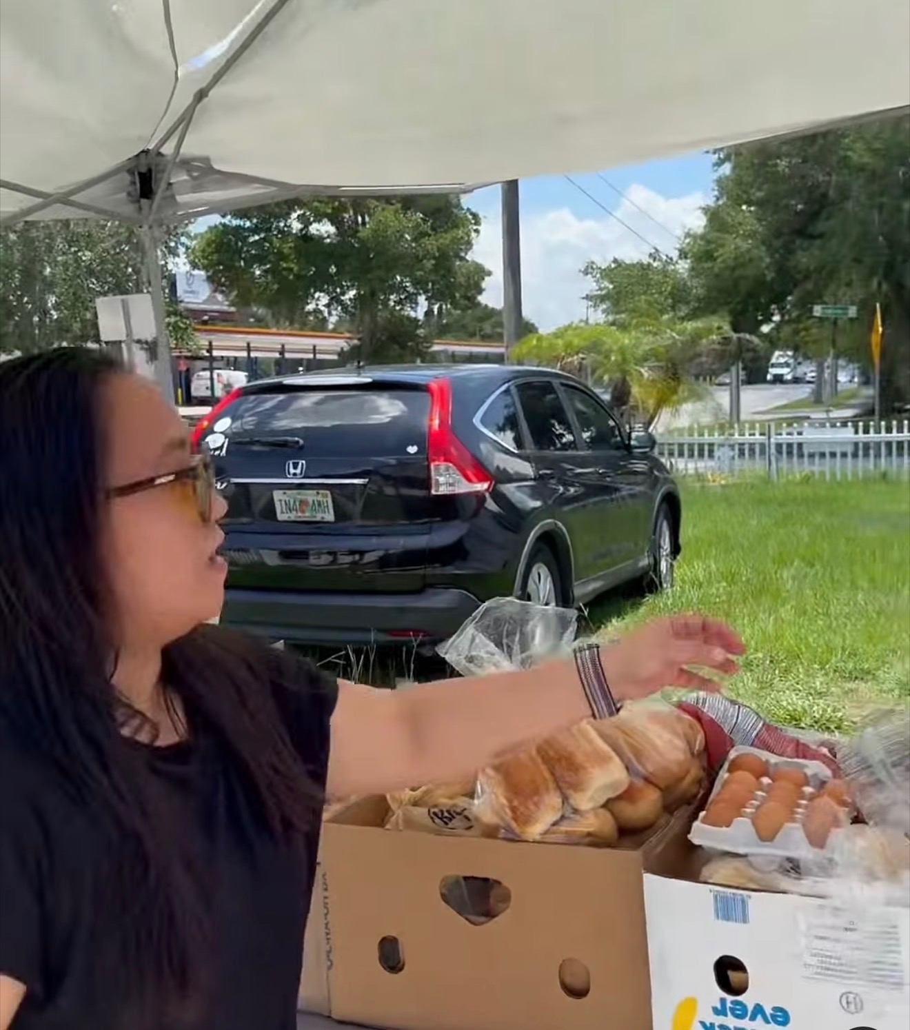 A volunteer under the white canopy reaching for boxes of fresh bread and eggs