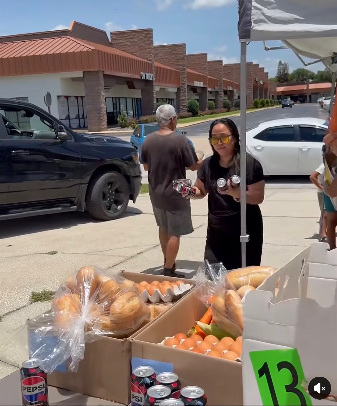 A volunteer behind a table stocked with bread and eggs, handing out groceries